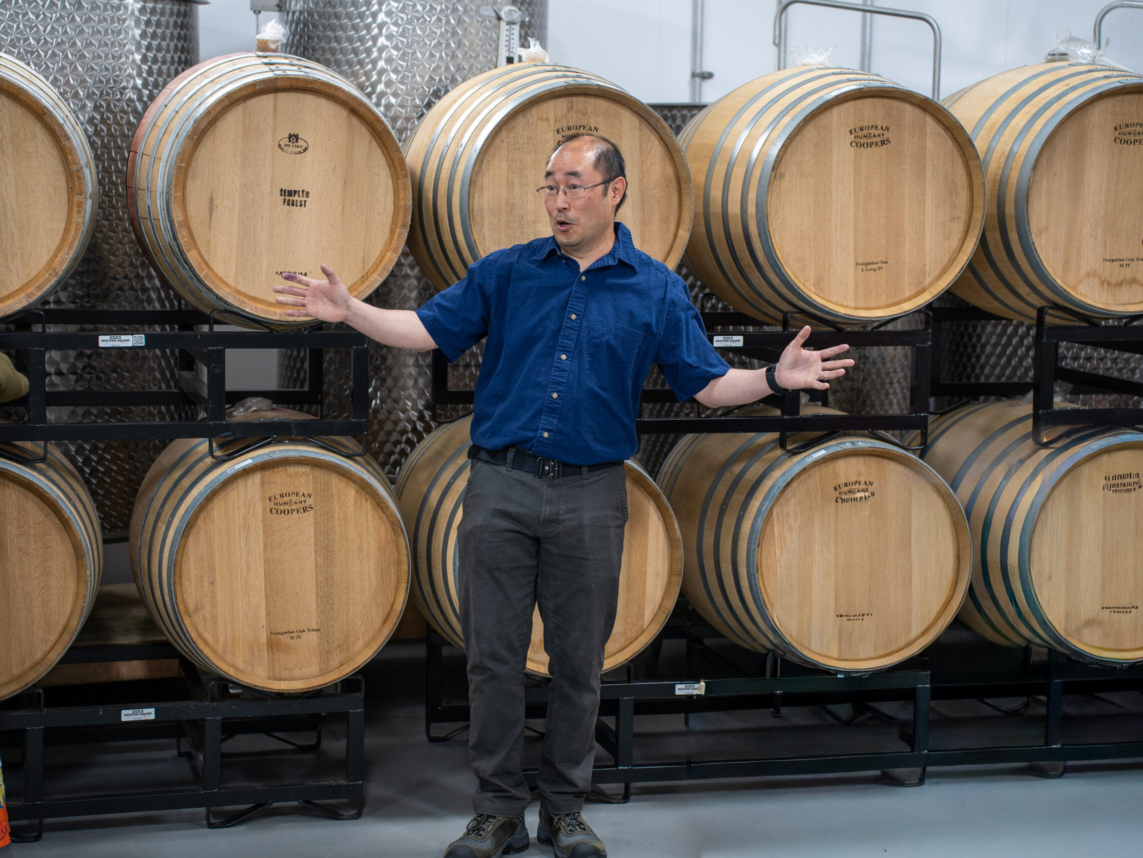 DSC00596 Winemaker in blue button down in front of wine barrels talking animated to people who are listening