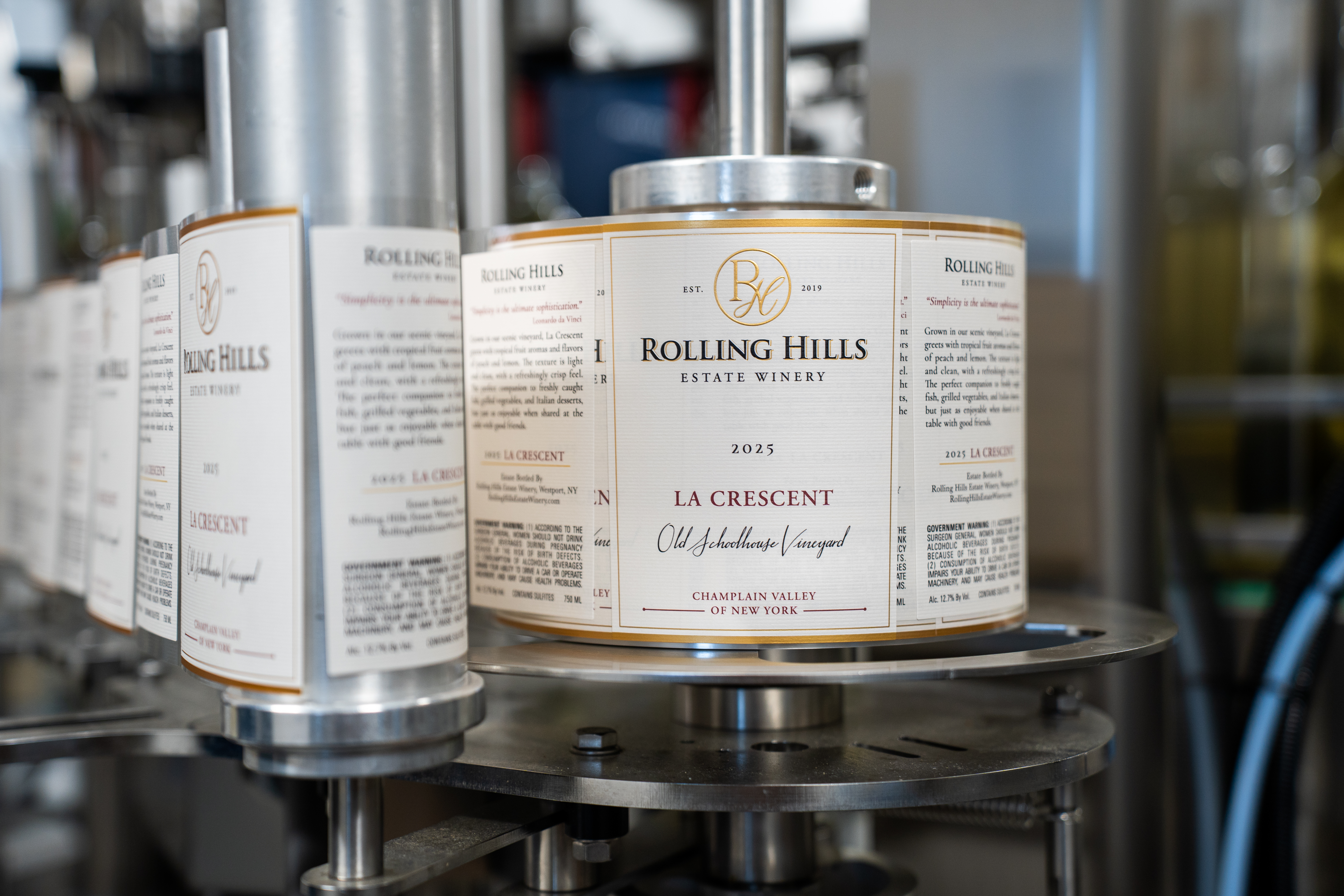 2025 La Crescent wine labels on a wine labeling machine. The label is off white with gold and maroon text