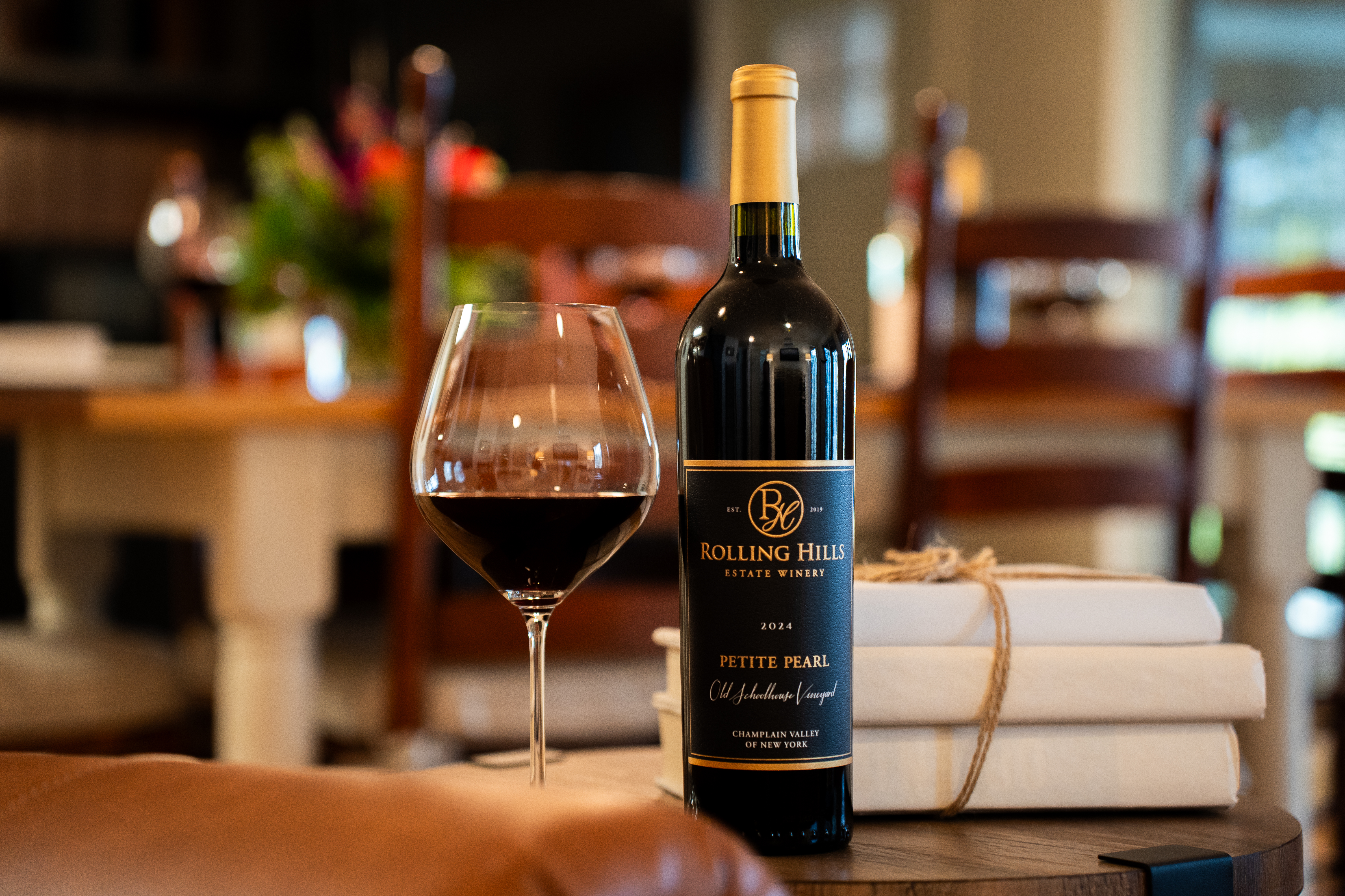 Wine bottle - 24 petite pearl on an endtable with a glass of red wine and a dining room table behind in background